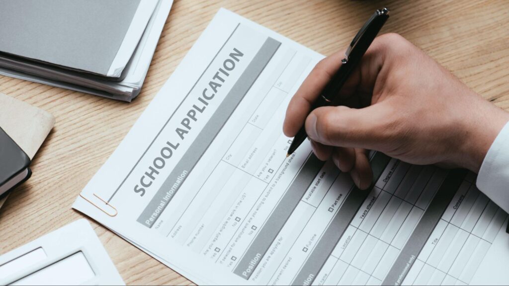 Parent completing a school enrollment application form with required documents.