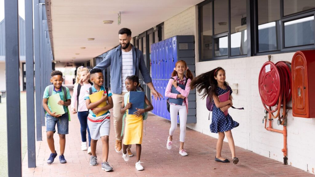 A teacher walking with a group of elementary students down a school hallway, representing a charter school in South Florida.