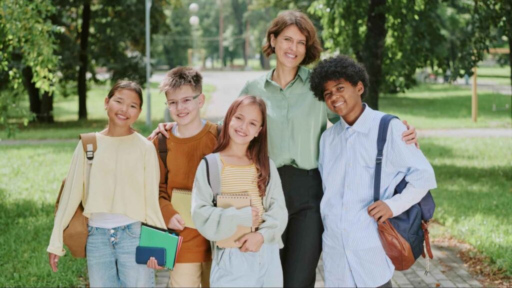 Teacher standing with a group of happy middle school students outdoors.