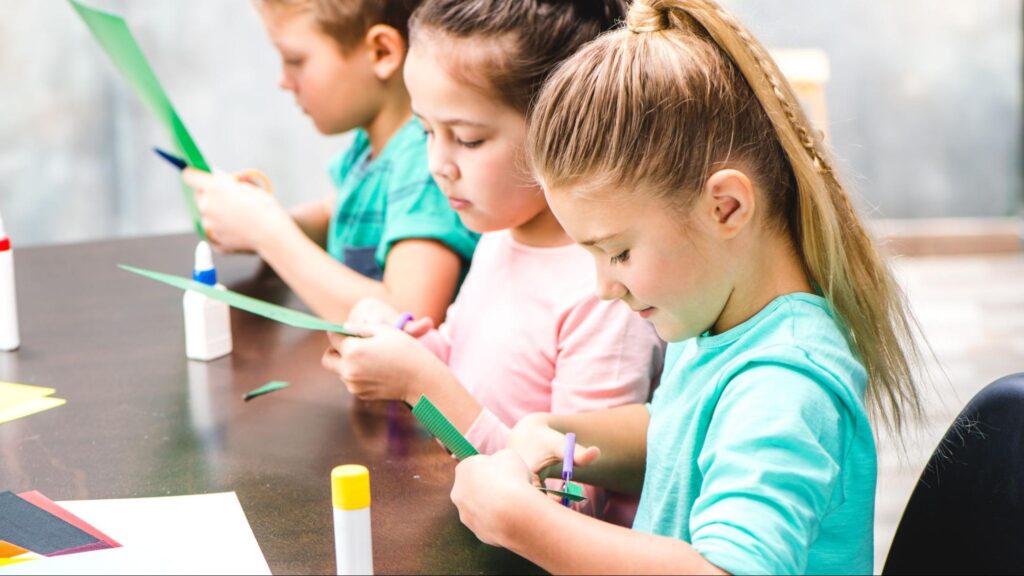 Children developing fine motor skills by cutting paper during an early learning activity in a Miami Pre-K classroom.