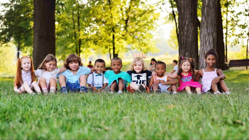 Group of diverse young children sitting outdoors together, demonstrating social development and school readiness in Miami early childhood programs.