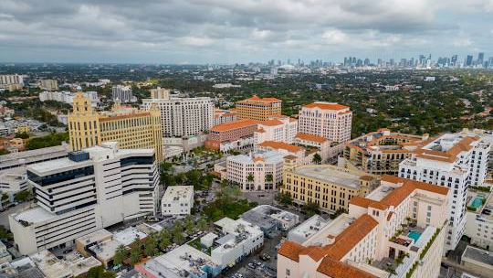The historic Mediterranean-style Giralda Tower in Coral Gables seen through green tree branches, representing the unique architectural charm of the neighborhood.