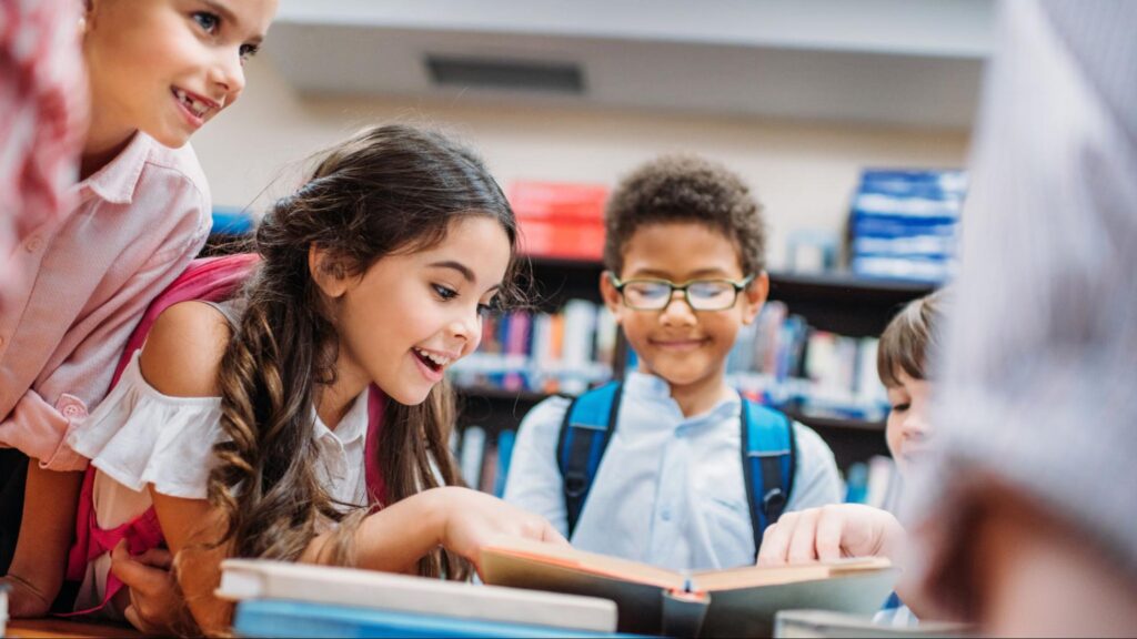 A group of young students excitedly looking at a book in a Coral Gables school library, highlighting the elite academic environment and focus on education in the area.