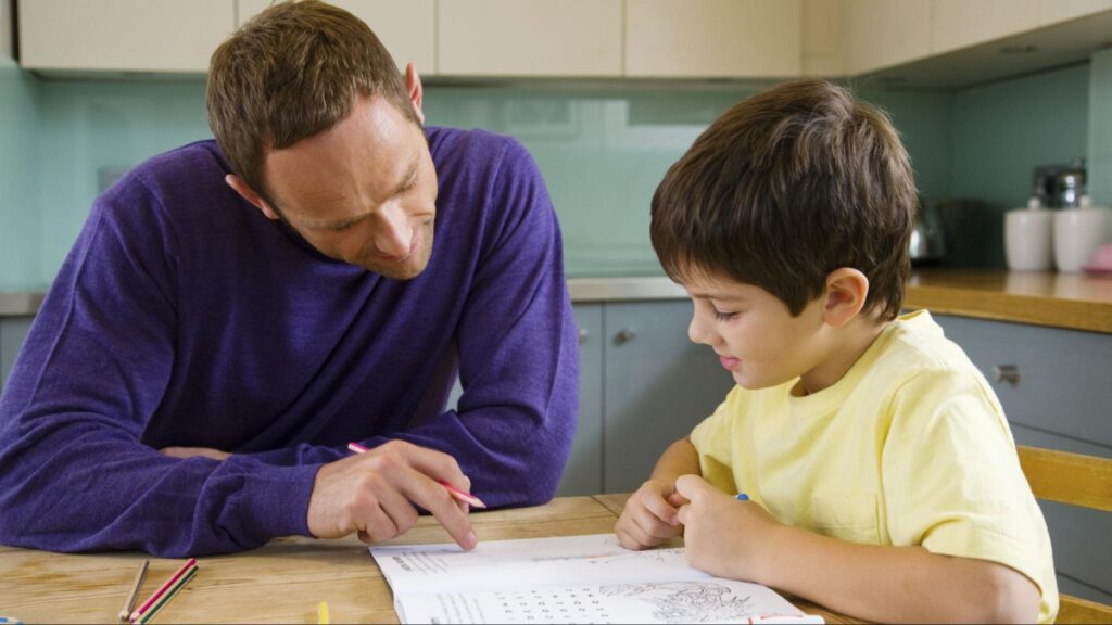 A father helping his young son with homework and early academic preparation at the kitchen table.